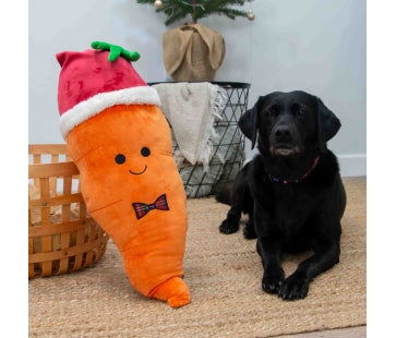 Ancol Giant Karl Carrot orange plush dog toy wearing a red-and-white Christmas hat and tartan bow tie, pictured beside a black Labrador.