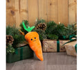 Ancol Mini Katie Carrot dog toy, a small orange plush carrot with green leaves and a smiling face, standing beside Christmas presents.