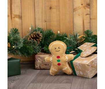 Ancol Georgia Gingerbread dog toy with a golden-brown body, white icing-style outlines and red and green buttons, pictured beside Christmas presents.