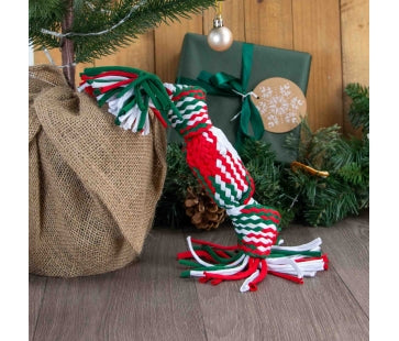 Ancol Squeaky Christmas Cracker Rope dog toy with red, green and white woven sections and tassels at both ends, beside Christmas presents.