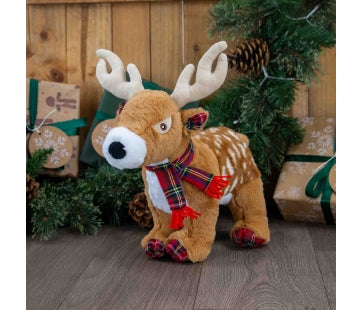 Ancol Stanley Stag brown plush dog toy with white spots, pale antlers, a red tartan scarf and tartan feet, standing beside Christmas presents.