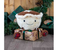Ancol Mikey Mince Pie plush dog toy with a cream fluffy pie body, brown lid, smiling face and long legs with tartan feet, sitting on a wrapped Christmas present.